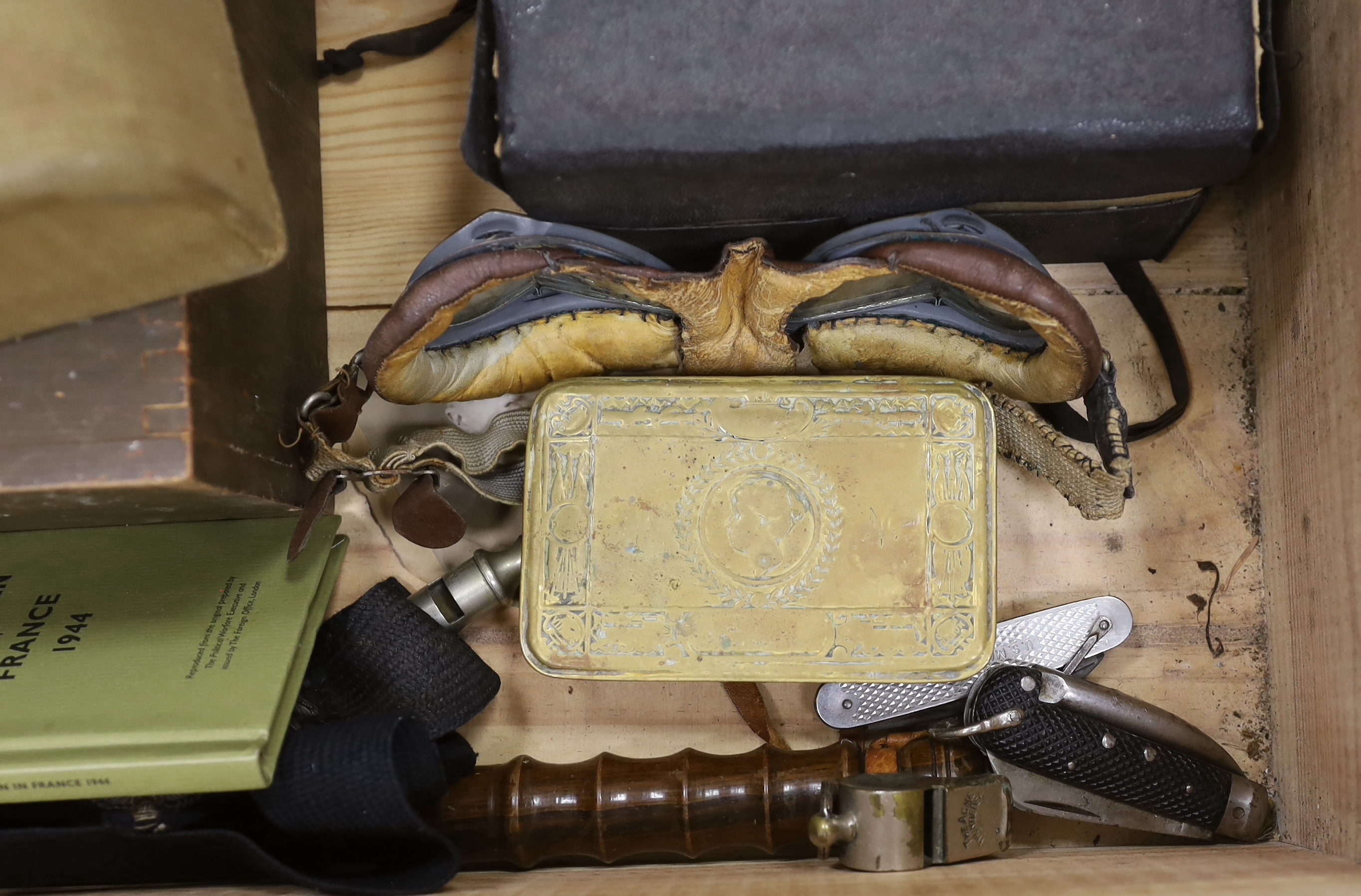 A quantity of militaria including a US Marine Corps penknife, another penknife, a pair of tank driver’s goggles, a Queen Mary Christmas tin, a box for a telephone attachment headgear, a truncheon, two hand axes, etc